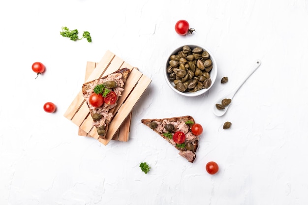 Appetizer bruschetta with tuna capers and tomatoes on wholemeal bread Italian cuisine Delicious breakfast or snack on a light background top view