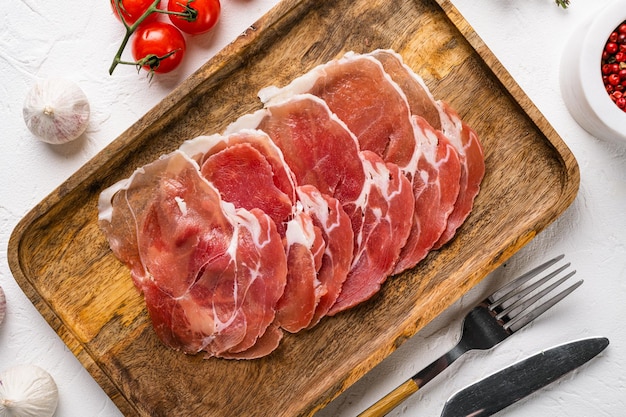 Appetizer from dry cured ham, prosciutto slices set, on white stone table background, top view flat lay