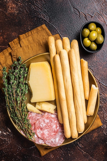 Appetizer plate with antipasti snacks grissini bread sticks salami olives and parmesan cheese Dark bakground Top view