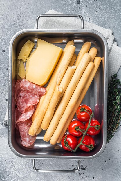 Appetizer platter with grissini bread sticks salami tomato and parmesan cheese Gray bakground Top view