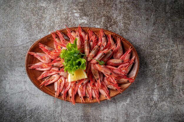 An appetizer in a restaurant, boiled shrimp on a wooden plate with lemon and herbs against a gray stone table