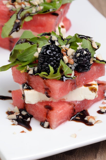 Appetizer  stacked slices of watermelon, feta, arugula, blackberry sauce and nuts