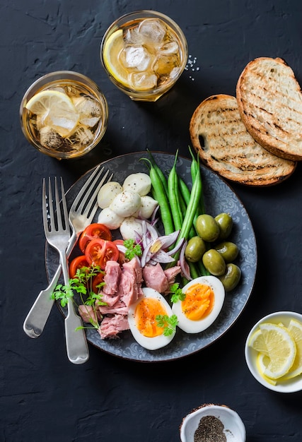 Appetizer table plate of canned tuna green beans mozzarella cheese tomatoes boiled egg olives grilled bread and two glasses of white wine