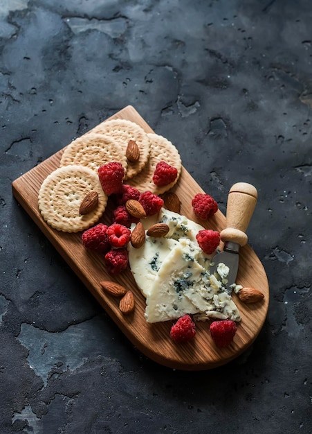 Appetizer tapas aperitif board blue cheese crackers nuts raspberries on a wooden board on a dark background top view
