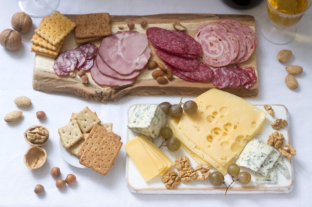 Appetizer of various types of sausages, meats, cheeses and crackers on a wooden board, served to wine.