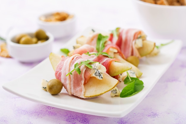 Appetizer with pear, blue cheese, prosciutto ham and toast for holidays on a white plate.