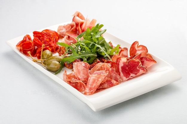 Appetizers of Italian sausages Prosciutto chorizo pancetta and salami Capers arugula and sundried tomatoes On white background