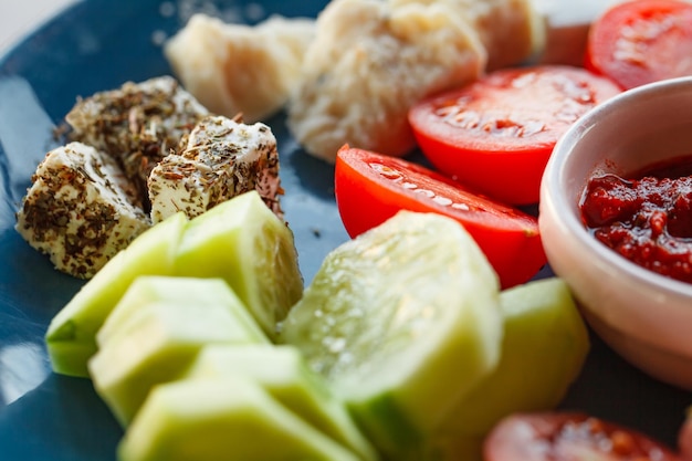 Appetizers snacks cheeses sliced cucumbers and tomatoes hot sauce on plate selective focus