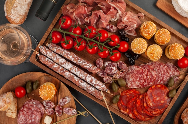 Appetizers table with diferents antipasti, cheese, charcuterie, snacks and wine. Mini burgers, sausage, ham, tapas, olives, cheese and baguette over grey concrete surface. Top view, flat lay