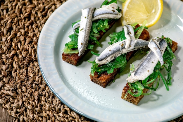 Appetizers tapas pickled anchovies or sardines fillet Wakame seaweed salad on toasted rye bread