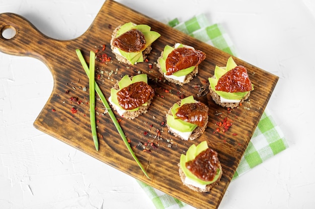 Фото Закуски с сыром авокадо и сушеными помидорами на доске концепция здорового питания