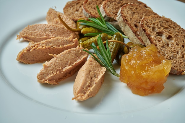Appetizing antipasti - goose paste with jam, rosemary and rye bread in white plate on wooden table/