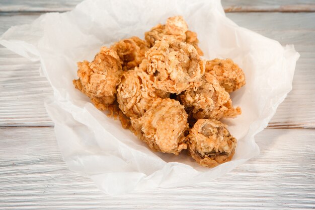 Appetizing baked breaded chicken in paper on white wooden table, flat lay. American fast food, tasty snack, traditional cuisine.