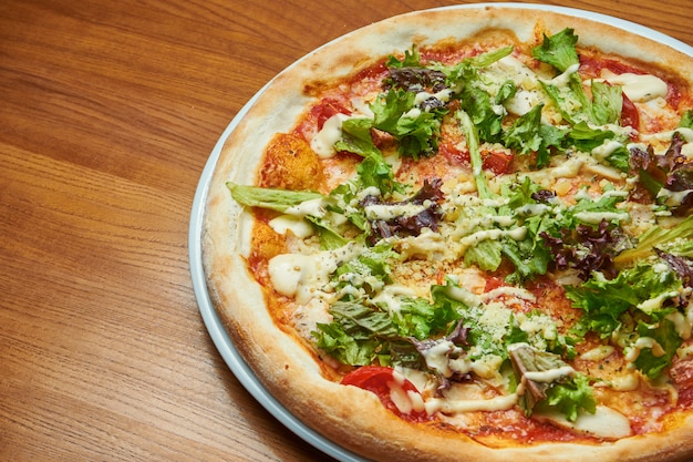 Appetizing baked Italian pizza with cream sauce, lettuce, chicken and parmesan on a white plate on a wooden table. Pizza caesar