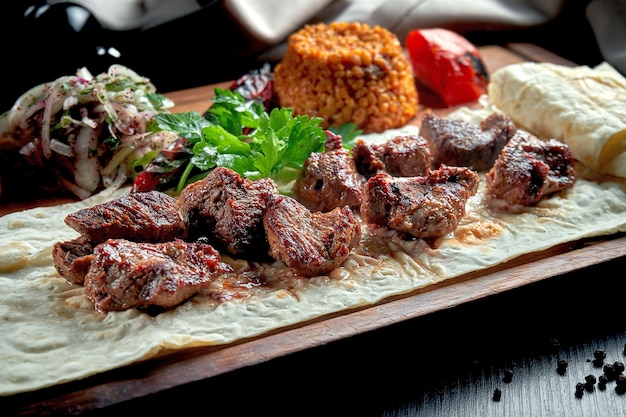 Appetizing beef kebab with grilled vegetables, bulgur and pickled onions on a wooden board