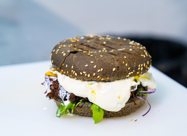 Appetizing black bun burger with fried egg Brown bread for hamburger with sesame seeds on white background Delicious fast food closeup