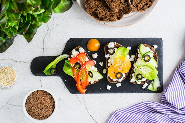 Appetizing bruschetta with feta cheese and vegetables on rye bread on a slate board Top view