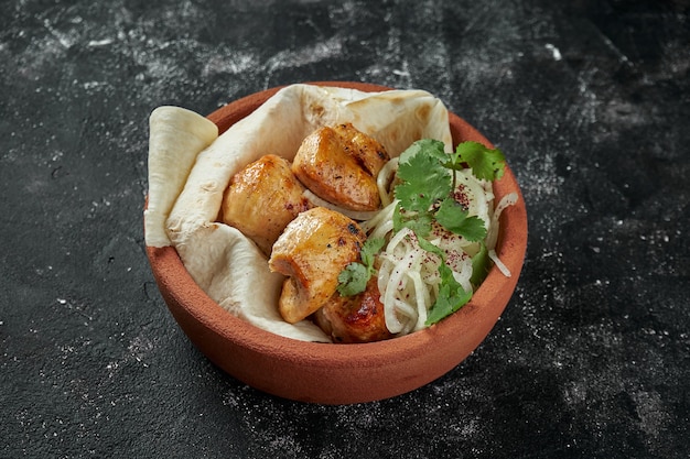 Appetizing chicken Shashlik or kebab with pickled onions and lavash in a ceramic bowl on dark table