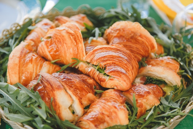 Appetizing croissants with meat and cheese filling and arugula in a woven rustic basket.