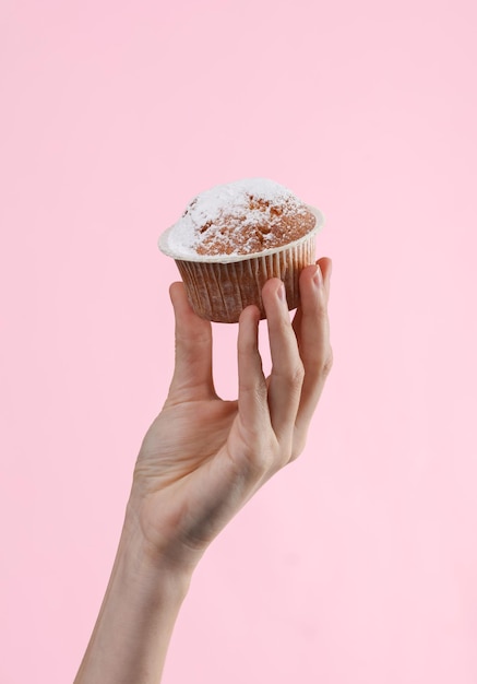 ピンクの背景に女性の手で作られたおいしいカップケーキやマフィン