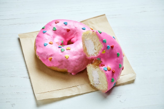 Appetizing donut with pink icing and strawberry filling on craft paper on a wooden table. Cut donut. Classic American dessert pastry