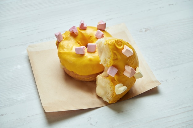 Appetizing donut with yellow icing and mango filling on craft paper on a wooden table. Cut donut. Classic American dessert pastry