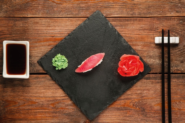 Appetizing fresh nigiri with tuna served on black slate, on wooden rustic table, flat lay. Japanese national seafood, healthy food.