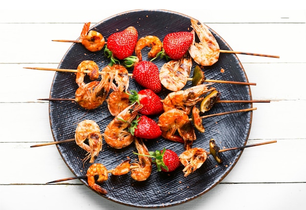 Appetizing grilled shrimps on wooden skewers with strawberries.Prawns bbq