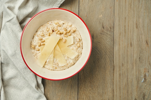 Appetizing and healthy breakfast - oatmeal with parmesan cheese in a bowl on a wooden surface. Close up. Copy space