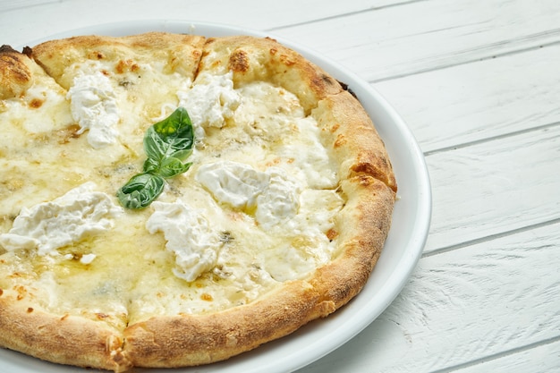 Appetizing, homemade 4 cheese pizza with blue cheese, mozzarella, parmesan and strachatella on a white plate on a white