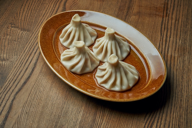 Appetizing homemade khinkali with different fillings (minced meat, cheese, vegetables or spinach) in a brown plate on a wooden surface. Traditional Georgian cuisine. Georgian dumplings