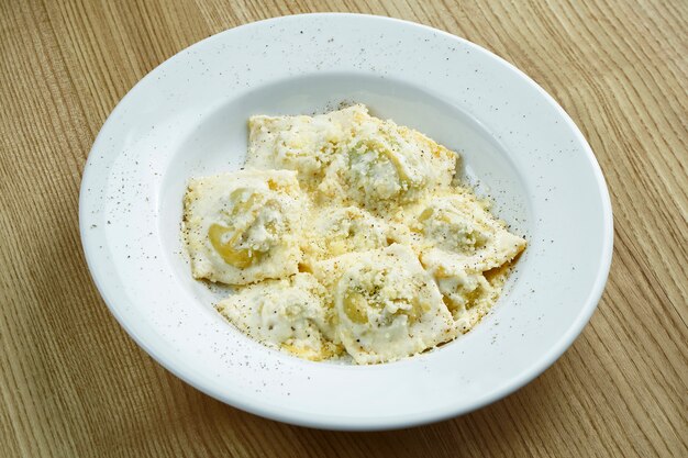 Appetizing and homemade ravioli stuffed with mushrooms or meat and ricotta cheese on a white plate on a wooden surface