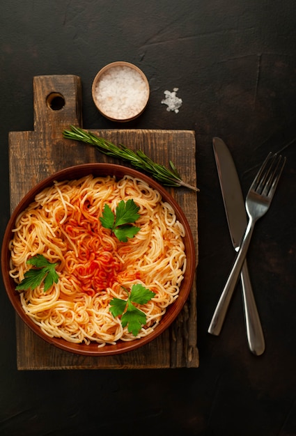 食欲をそそるイタリアのパスタスパゲッティトマトソース、プレートにパルメザンチーズ、コンクリート背景にまな板。上からの眺め