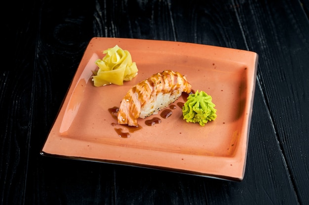 Appetizing Japanese nigiri with smoked salmon and unagi sauce, served in a plate with ginger and wasabi on a black wooden background