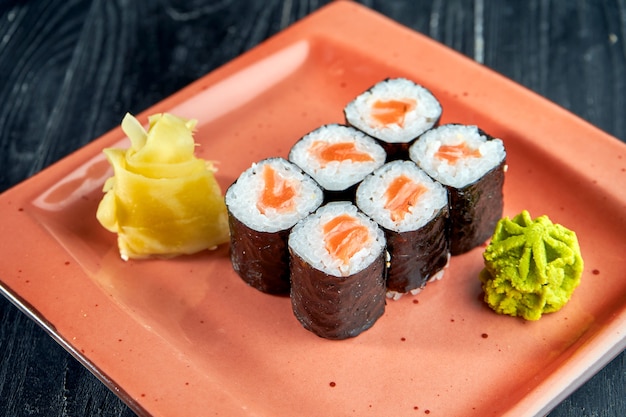 Sushi giapponese appetitoso - maki con salmone servito in un piatto con zenzero e wasabi su una superficie di legno nero. cucina giapponese