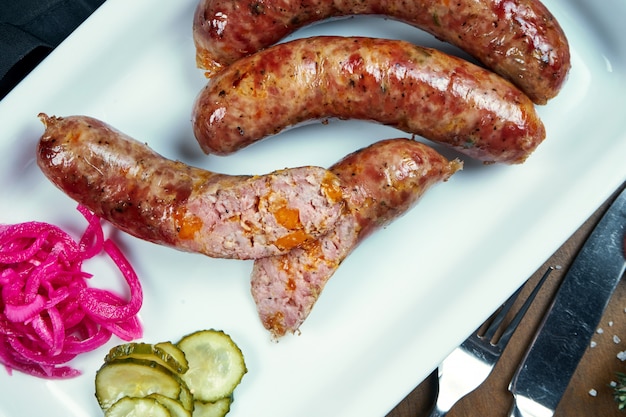 Appetizing juicy pork minced sausage baked in a smoker with cheddar in a white plate with canned vegetables. German beer snack