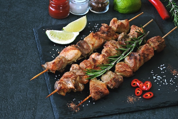 Appetizing kebab with spices, chili and lime. Fragrant pork skewers on a stone board.