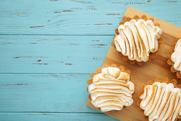 Appetizing lemon cupcakes with white cream on wooden board on blue background. Holiday, surprise, birthday, Valentine's Day.