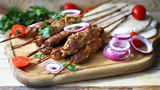 Appetizing lula kebab on wooden sticks with onion rings and herbs