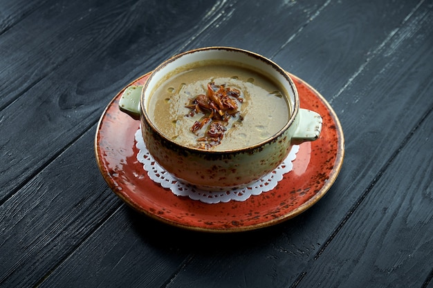 Appetizing mushroom cream soup with olive oil and fried mushrooms, served in a bowl on a black background.