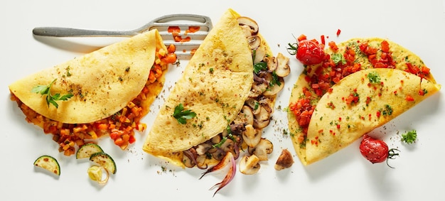 Appetizing omelets with vegetables and mushrooms on white table