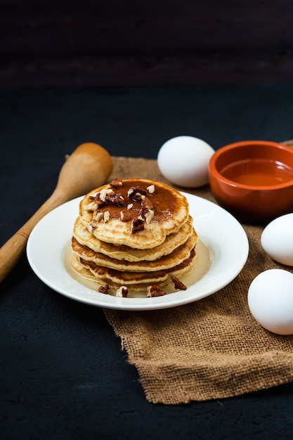 Pancakes appetitosi con miele e noci su un tavolo scuro con uova e una ciotola di miele menu, ricetta del ristorante. servito in