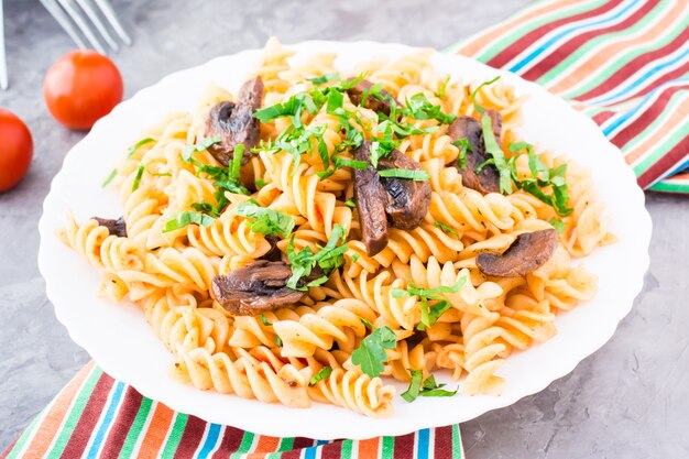 Appetizing pasta with fried mushrooms and fresh herbs on a plate