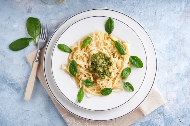 Appetizing pasta with sauce pesto and spinach in plate on light blue stone table Top view