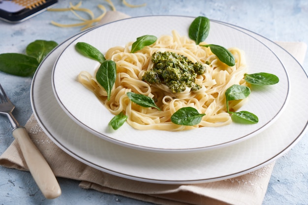 Appetizing pasta with sauce pesto and spinach in plate on light blue stone table.