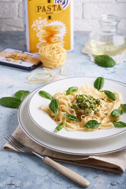 Appetizing pasta with sauce pesto and spinach in plate on light blue stone table