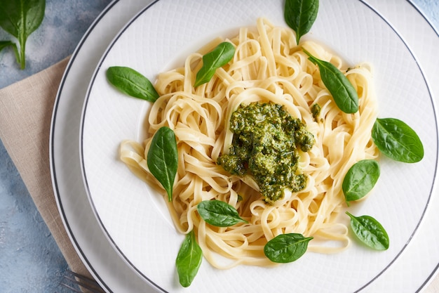 Appetizing pasta with sauce pesto and spinach in plate on light blue stone table