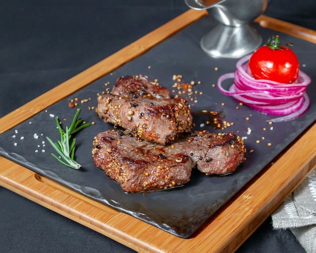 Appetizing pieces of meat on serving plate served with grilled tomato and fresh onions on dark