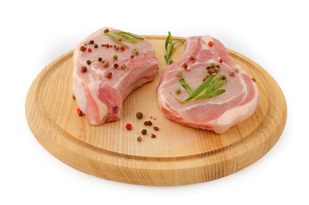 Appetizing pieces of pork chops meat with rasmarin and pepper on a round cutting board isolated on a white background Side view