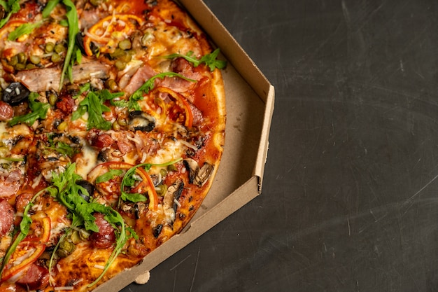 Appetizing pizza with smoked sausages bacon meat tomato cheese arugula cardboard boxes for delivery on black dark . With copyspace 